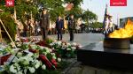 Zdjęcie z uroczystości obchodów 68 rocznicy Poznańskiego Czerwca. Na pierwszym tle wieńce kwiatów i płonący znicz. Przed nimi stoi trzech mężczyzn, dwóch ubranych w mundury salutuje. 
